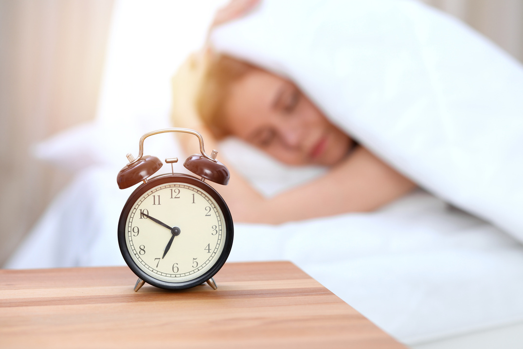 Alarm clock opposite of sleepy young woman. Early wake up, not getting enough sleep concept.